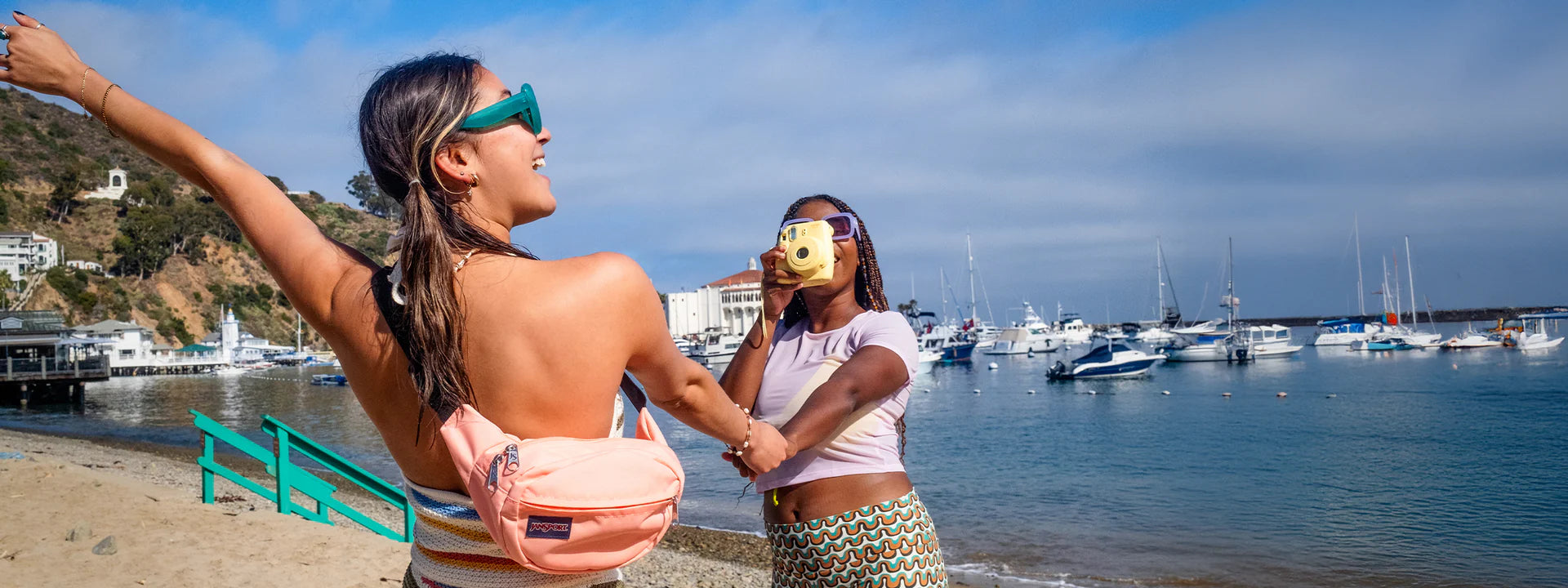 Two women on a beach with boats in the background