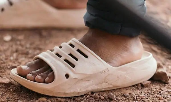 Close-up of a foot wearing a beige sandal on a dirt surface