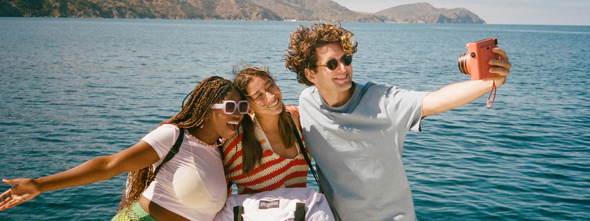Three friends taking a selfie on a boat with a scenic ocean view and islands in the background.