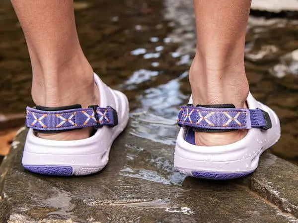 White sandals with purple straps on a stone surface near water