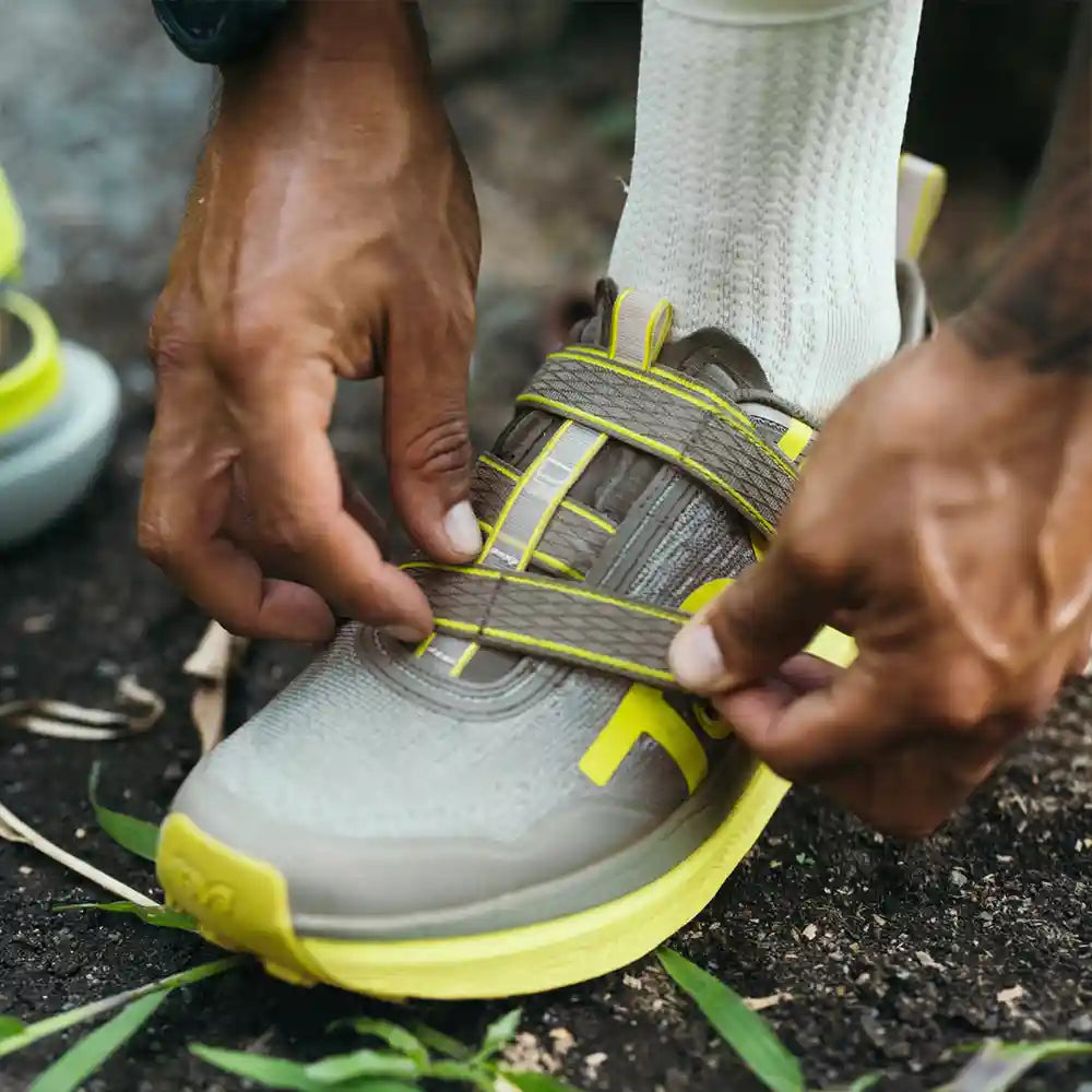 Person tying a gray and yellow running shoe outdoors