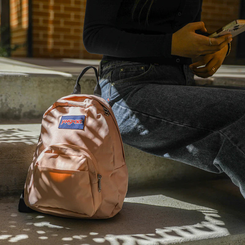 Person sitting on a bench with a beige backpack featuring a JanSport mini backpack.